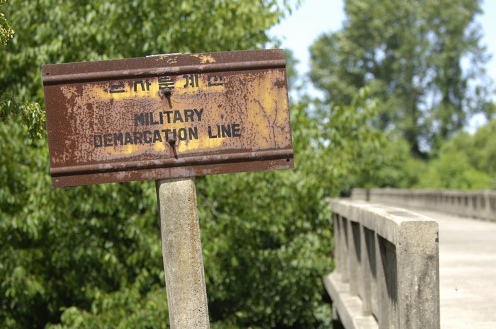 Rusted sign for Military Demarcation Line near bridge