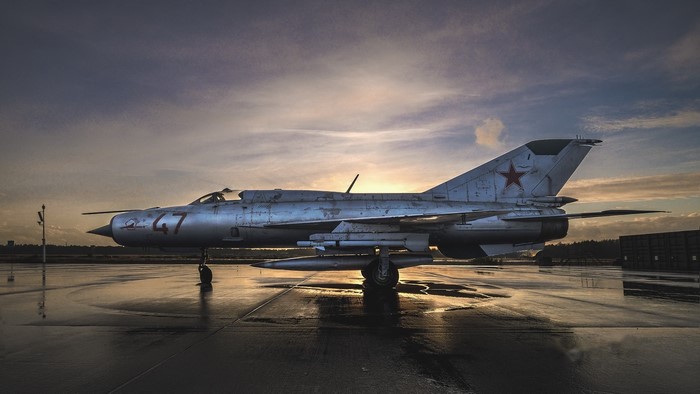 MiG-21 fighter jet on a wet tarmac at sunset