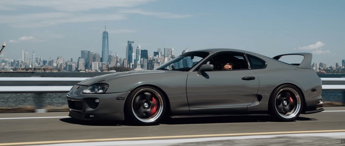 Gray Toyota Supra MK4 driving with New York City skyline