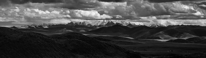 Monochrome panorama of snowy mountain peaks under dramatic clouds
