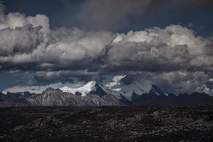 Dark clouds over snow-capped mountains and rocky foreground