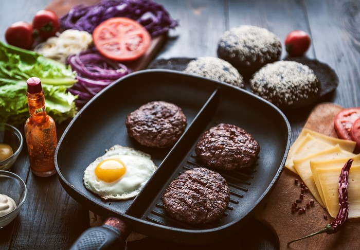 Burger patties and fried egg in a grill pan with ingredients