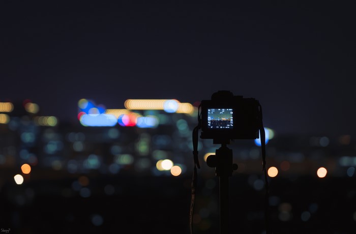Camera on tripod at night with city lights