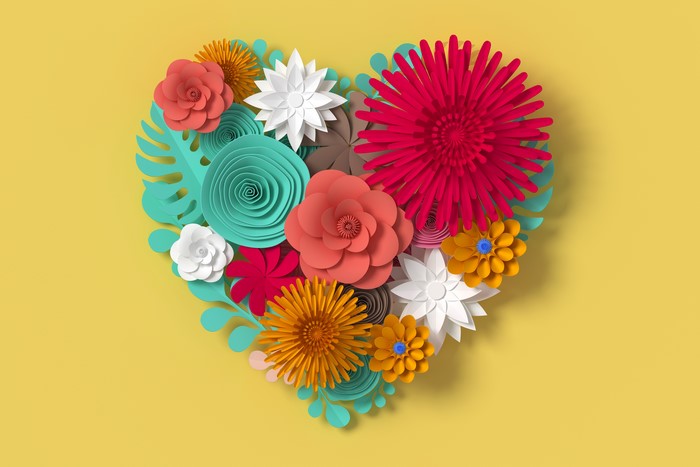 Heart shape made of paper flowers on yellow background