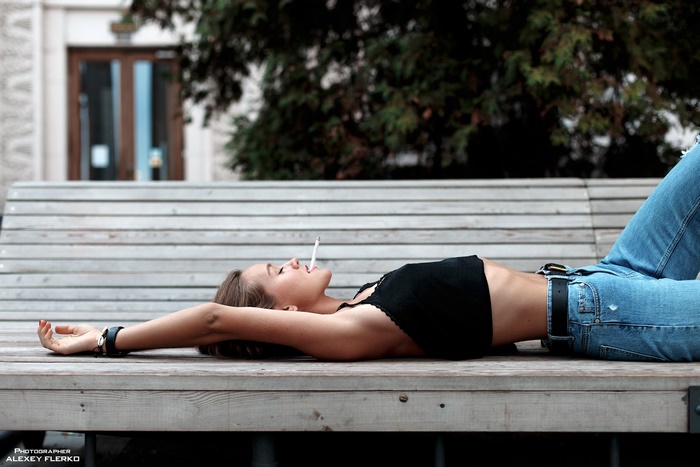Woman in black top and jeans smoking on a bench