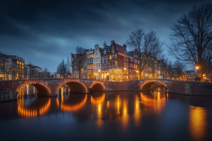 Amsterdam canal bridge at night with building reflections