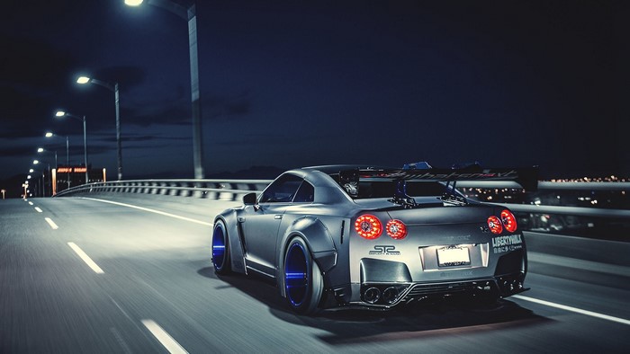 Nissan GT-R with Liberty Walk body kit and colored wheels on a bridge at night