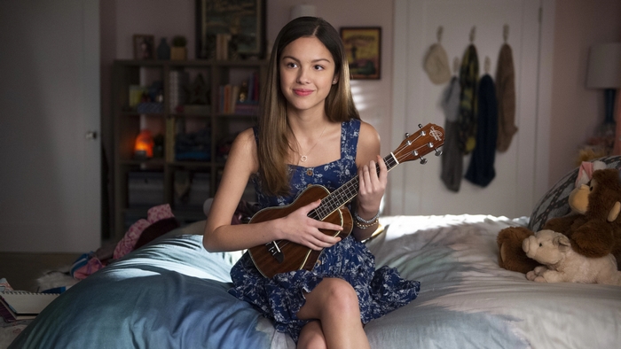 Olivia Rodrigo holds a ukulele while sitting on a bed
