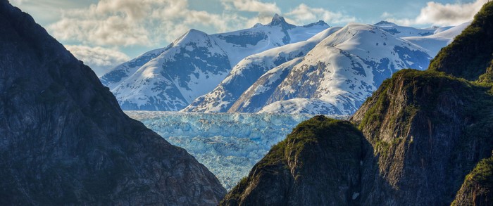 Glacier between snow-capped mountains and rocky slopes