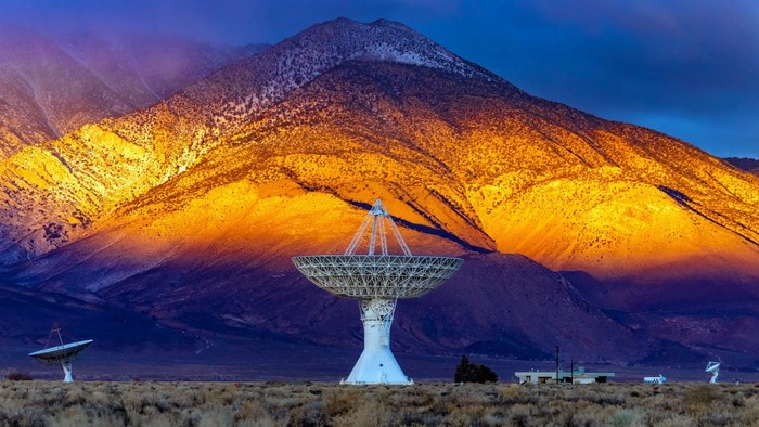 Radio telescopes in front of sunlit mountains in USA