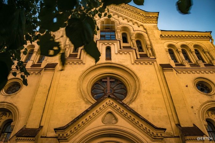 Low-angle view of a yellow church facade with a cross window