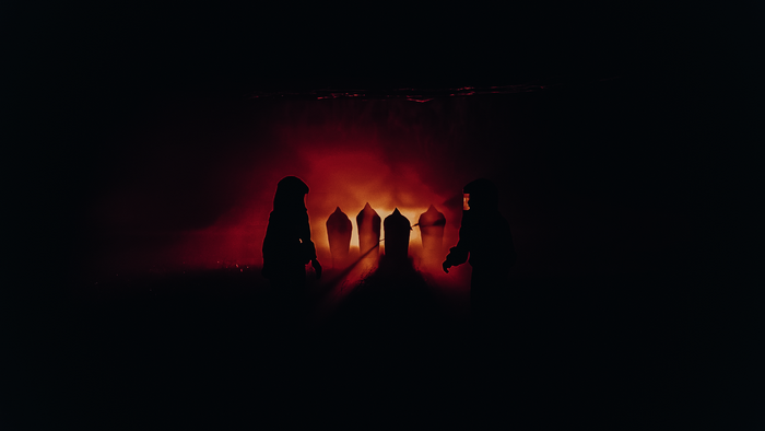 Two figures in silhouette stand before glowing tomb-like structures