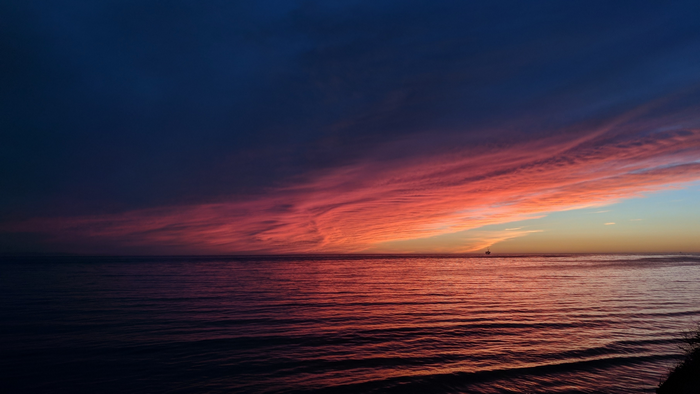Sunset over the ocean with colorful clouds and a distant ship
