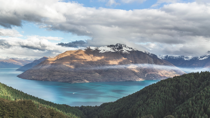 Snow-capped mountains overlooking a turquoise lake with a boat