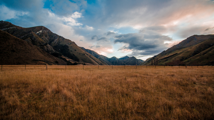 Mountains and dry grass field under cloudy sky