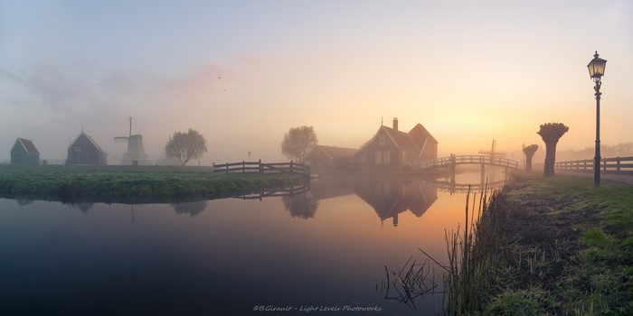 Misty Dutch landscape with windmills and canal at dawn