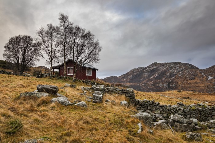 Red cabin in a rocky, grassy landscape with mountains