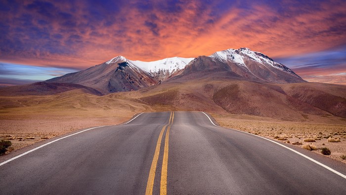 Road leading to snow-capped mountains under a colorful sky