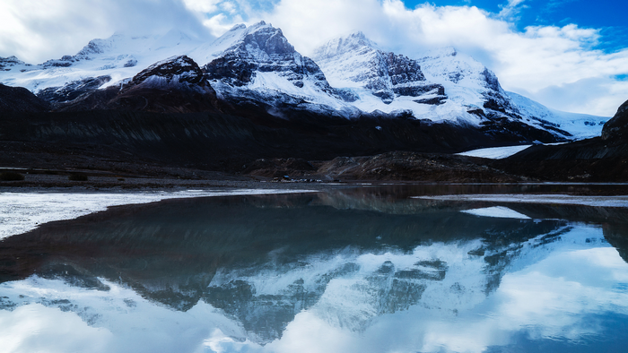 Snow-capped mountains reflected in a calm lake under a cloudy sky