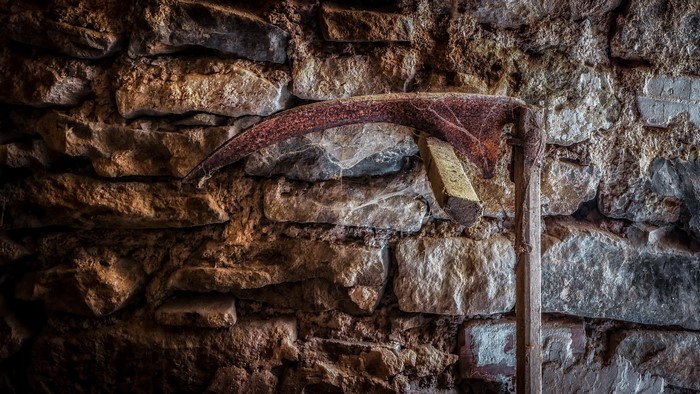 Old rusty scythe leaning against a stone wall
