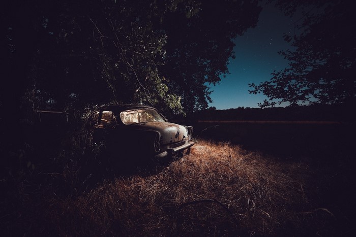 Abandoned car at night under starry sky