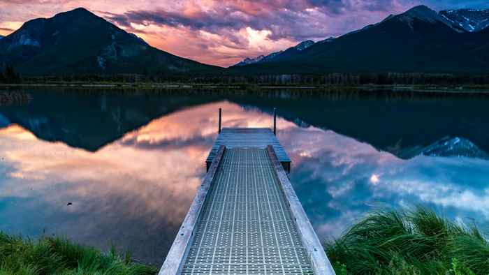 Wooden dock on a lake with mountains at sunset