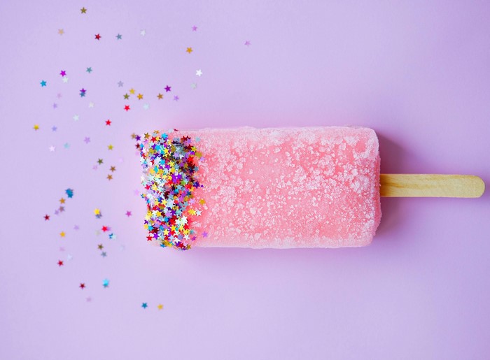 Pink popsicle with colorful star sprinkles on purple background
