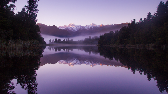 Misty mountains reflected in a calm lake at dawn