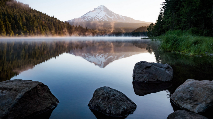 Snowy mountain reflected in a misty lake with rocks and trees