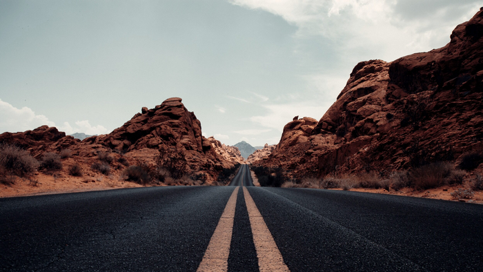 Road through red rocks under a cloudy sky
