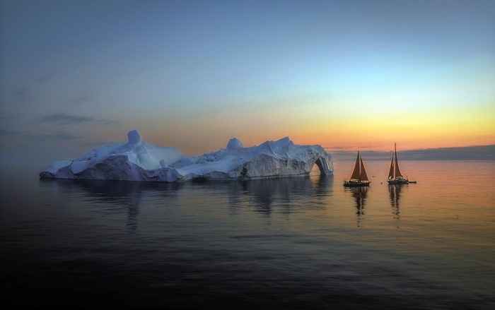 Iceberg and sailboats in Greenland at sunset
