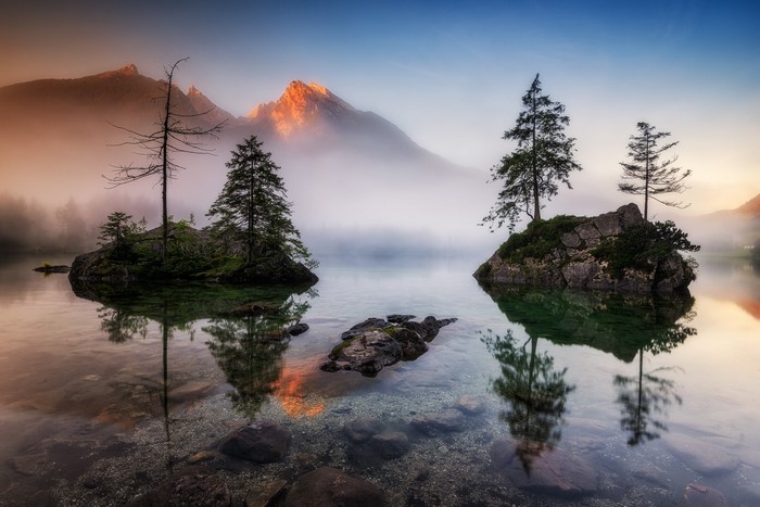 Misty mountain lake with islands and trees at sunrise