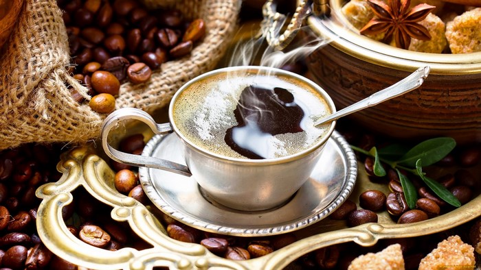 Steaming cup of coffee with beans and sugar