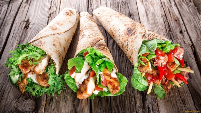 Three chicken wraps with salad and vegetables on a wooden table