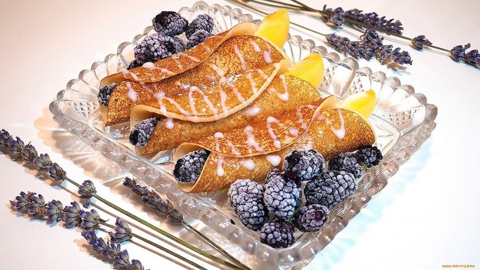Crepes with blackberries and lemon slices on a glass plate