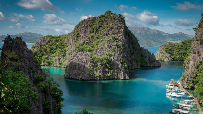 Rocky islands with lush vegetation in a turquoise bay with boats and a pier