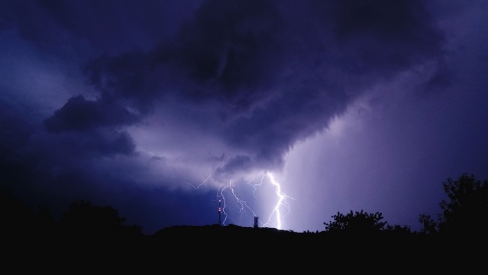 Lightning strikes a radio tower during a nighttime storm over hills