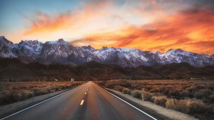 Road leading to snow-capped mountains at sunrise