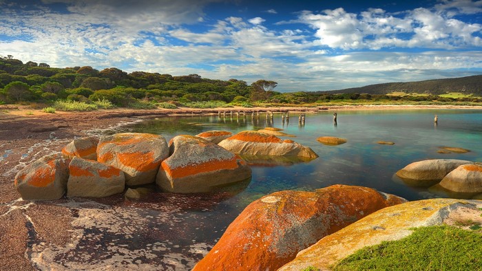 Orange-streaked rocks on a beach with calm water and green hills