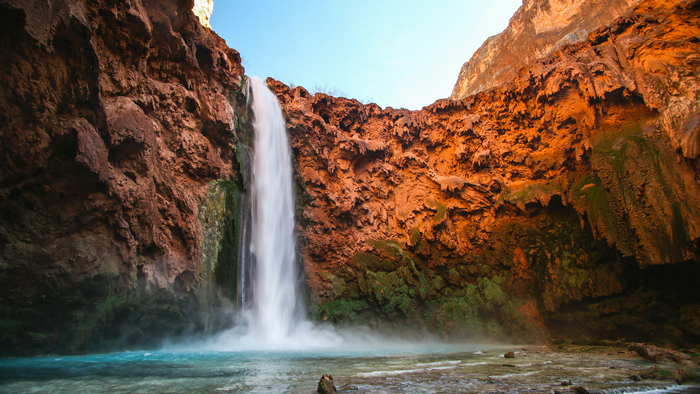 Waterfall cascading into a turquoise pool in a canyon