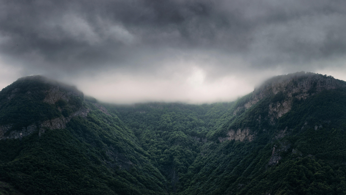 Misty mountains covered in green trees under stormy clouds