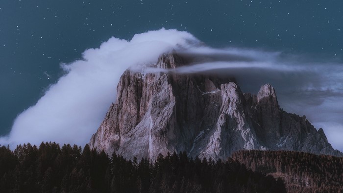 Mountain peak shrouded in clouds under a starry night sky