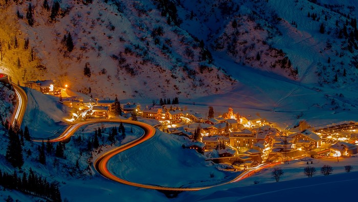 Snowy mountain village with winding road at night