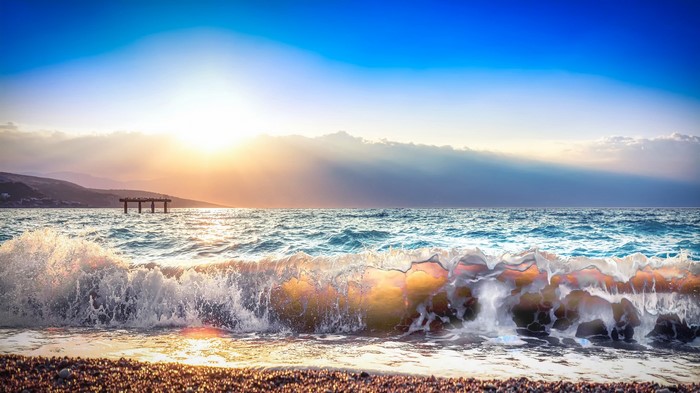 Ocean waves crashing on a beach at sunset with a pier