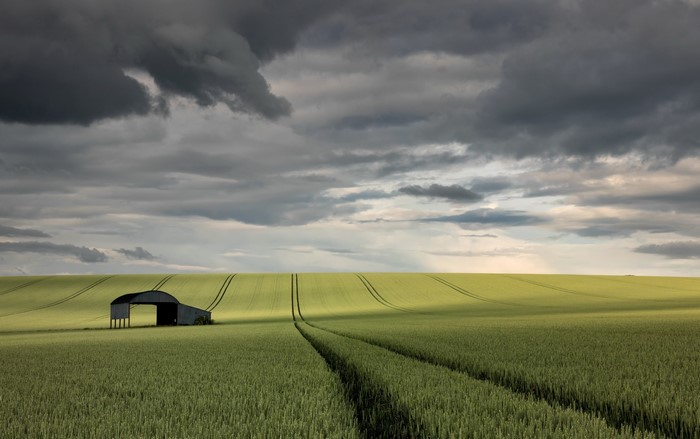 Barn in a green field under a cloudy sky