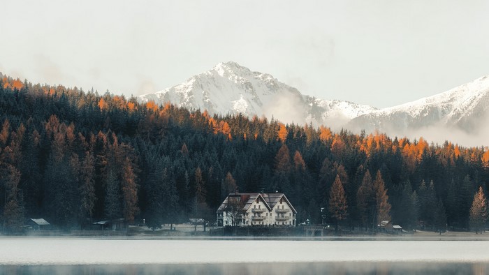 House by a lake with autumn forest and snowy mountains