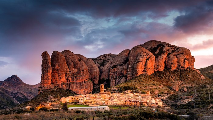 Village nestled at the base of rocky mountains at sunset