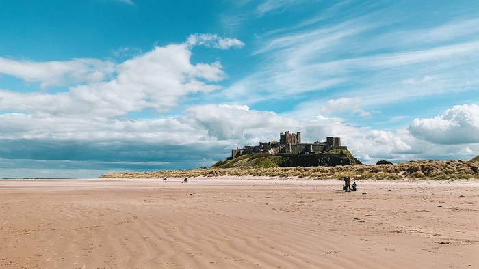 Bamburgh Castle on a sandy beach under a cloudy sky