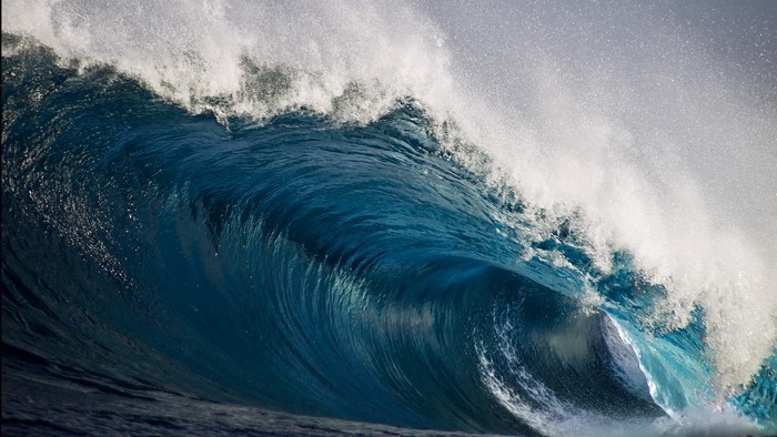 A large blue ocean wave crests and breaks