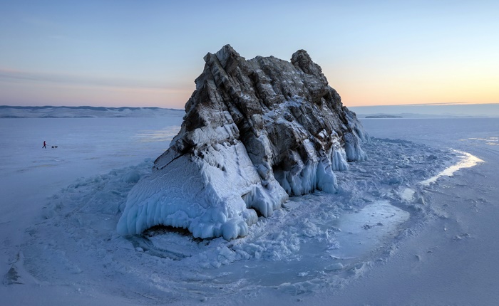 Person walking on frozen lake with rock formation